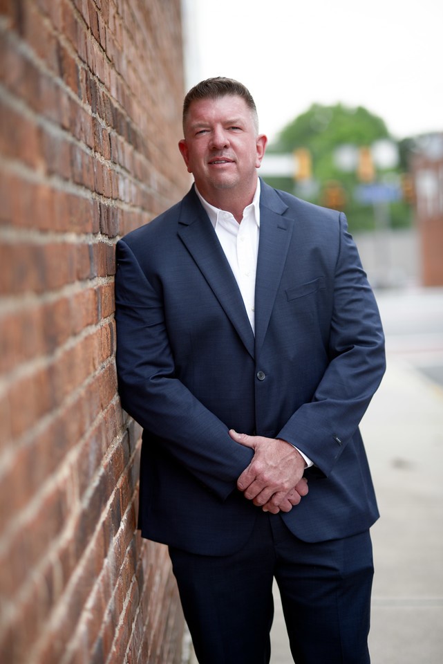 A man in a suit leaning against a brick wall.